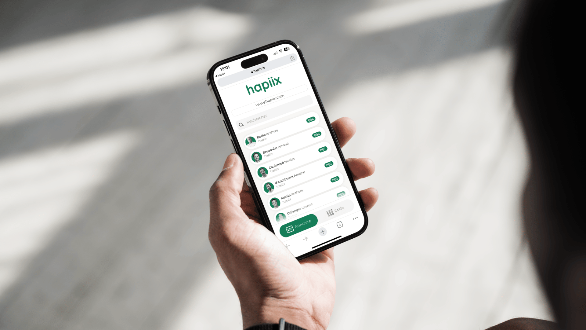 Un smartphone est tenu dans une main et l'annuaire en ligne de la solution hapiix est affiché.
