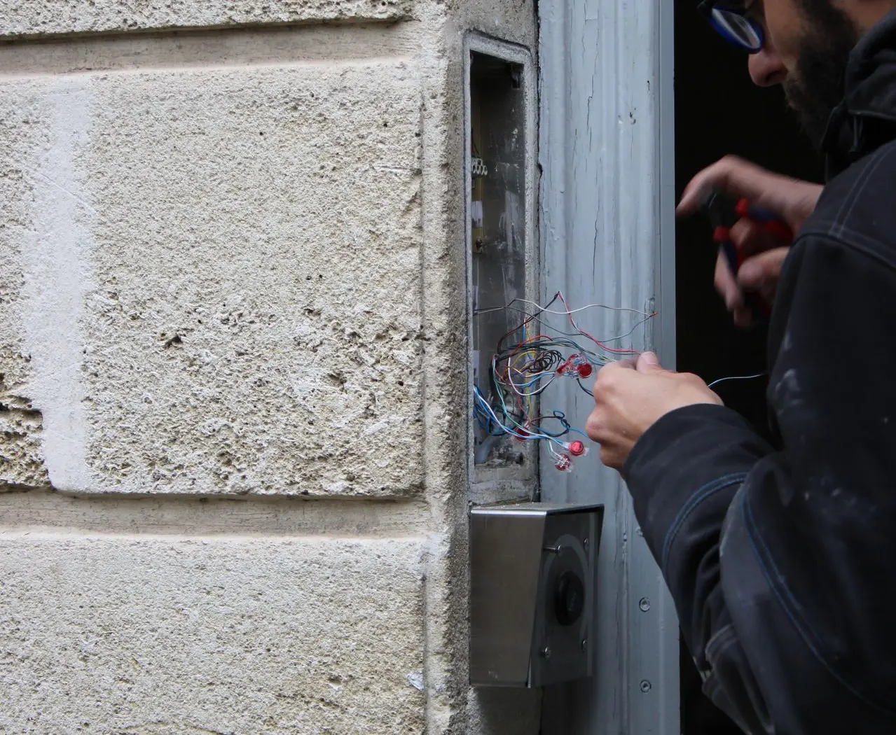 photo d'un installateur en train de désinstaller un interphone dont les câbles de l'ancien système sont apparents 