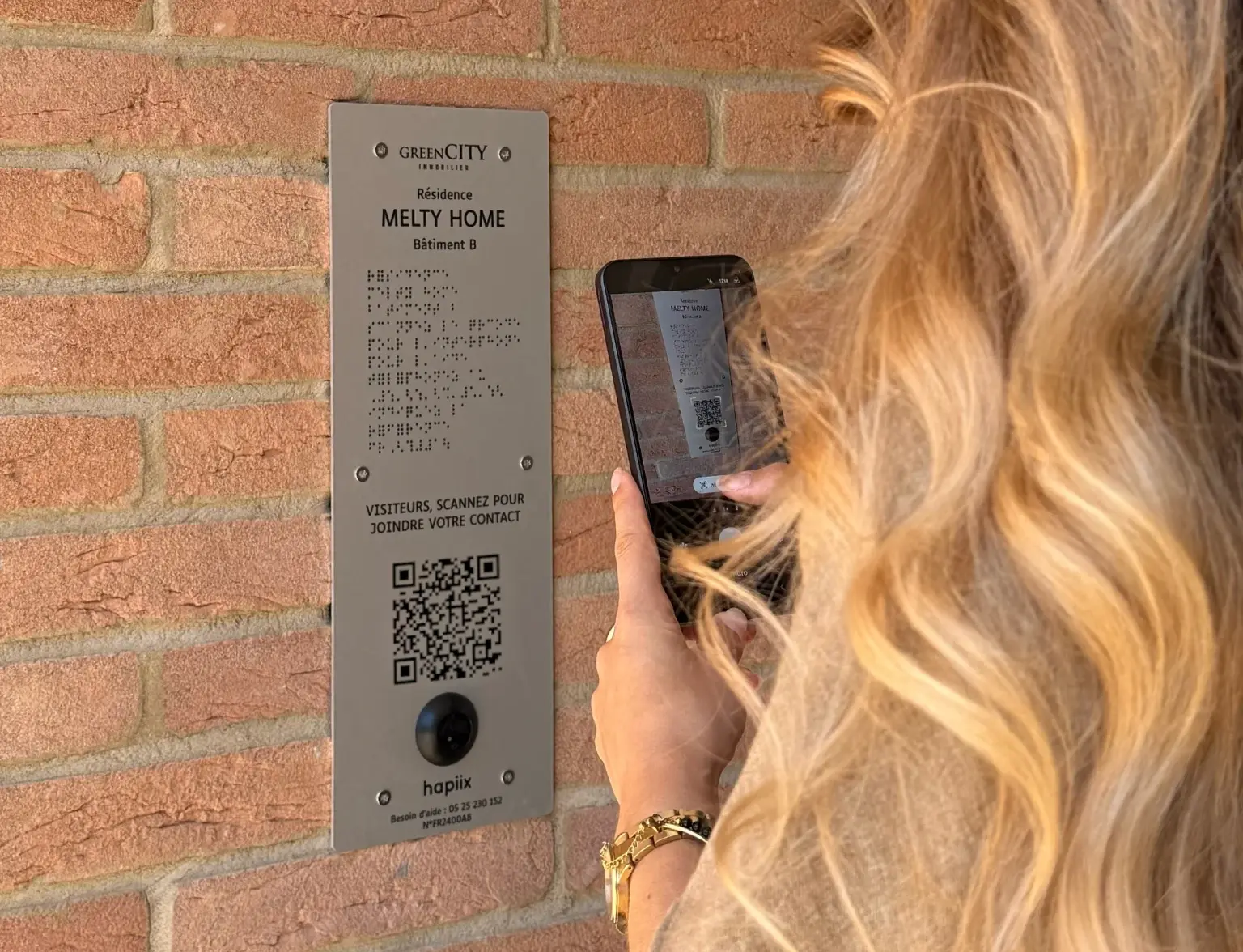 Photo d'une femme scannant un QR code sur une plaque d'interphone hapiix 